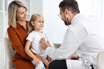 Fototapeta premium Doctor examining little girl with stethoscope and her mother in hospital