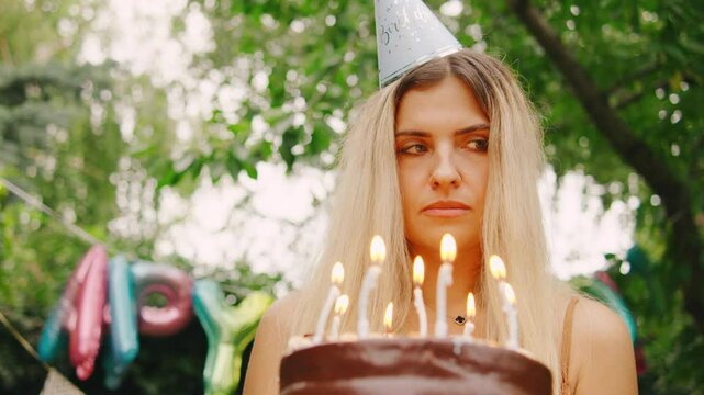A sad woman with party hat stands alone surrounded by festive birthday decorations, balloons, and flags, feeling disappointed that no one showed up to her party