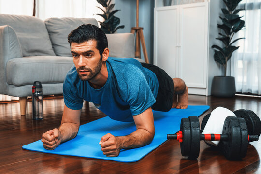 Athletic and sporty man doing plank on fitness mat during home body workout exercise session for fit physique and healthy sport lifestyle at home. Gaiety home exercise workout training.