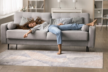 Happy relaxed young Latin woman resting on comfortable couch, lying on back with open arms, legs...