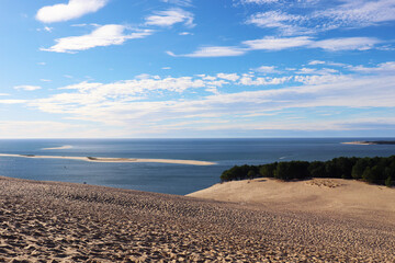 large sand dune with ocean and blue sky in the background