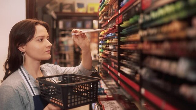 Dedicated female store clerk sorting vibrant pencils in art supply section. Young employee carefully managing art products with precision and focus