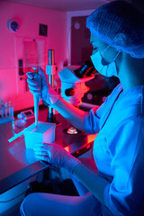 Female embryologist pipetting samples under dramatic colored lighting