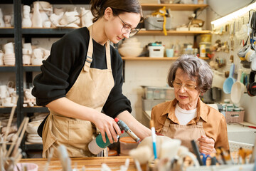 Young woman teaches elderly lady how to work with clay