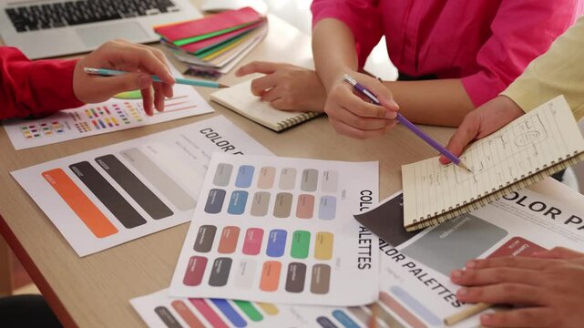 Slow motion hand closeup of two designer drafting new design layout on note book and choosing color with client oversee the project. Chromatic consultation at designer agency office. Variegated