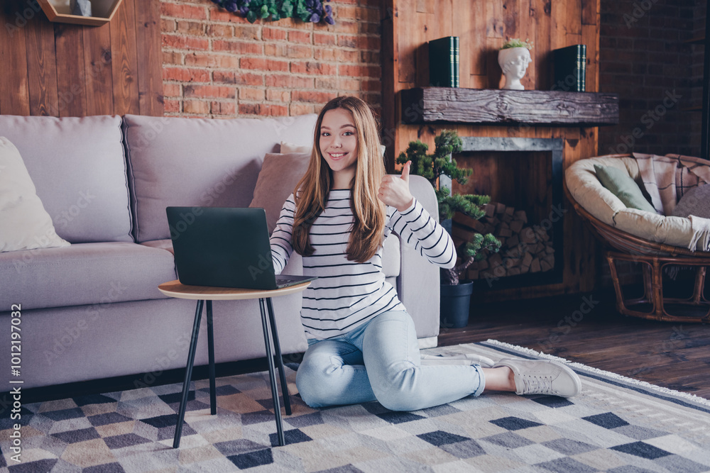 Poster Full length photo of attractive teen female sit floor netbook thumb up dressed striped outfit cozy day light home interior living room