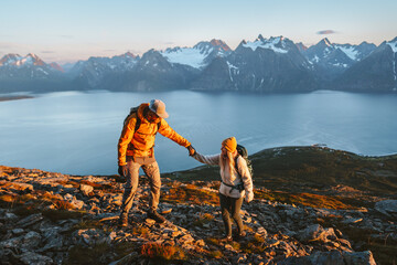 Couple hiking in mountains man giving helping hand woman, active vacations in Norway healthy lifestyle outdoor family adventure trip friends climbing in Lyngen Alps