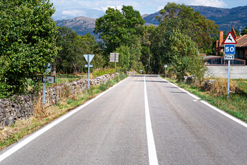 long and solitary road in the village with trees and mountains in the background