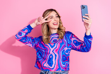 Selfie photo of cute dyed curly hair girl wearing bright stylish shirt using smartphone cover face v sign pose isolated on pink color background