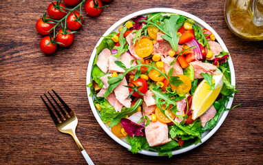 Fresh salad with canned tuna, tomatoes, onion, corn, paprika, lettuce and arugula. Rustic table background, top view