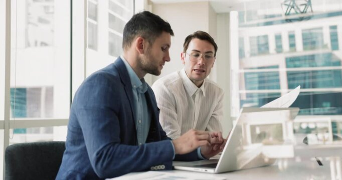 Two businessmen using laptop in conference room, evaluate effectiveness of marketing campaign, prepare presentation for meeting, discuss financial report and budget allocation, developing new ideas