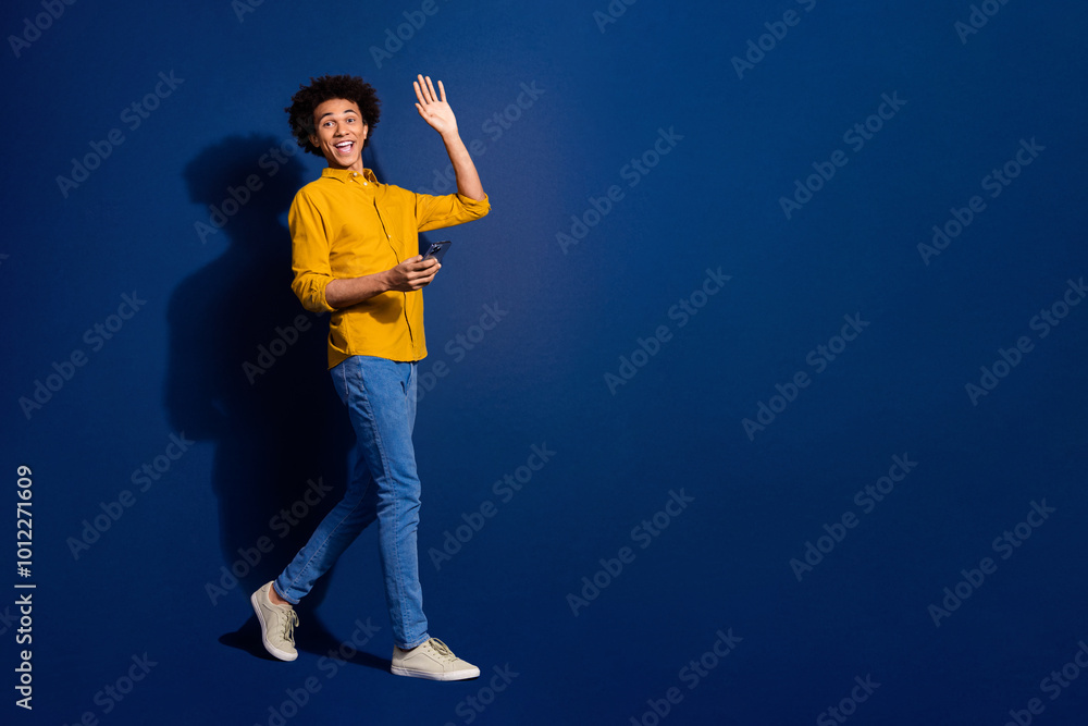 Poster Full size photo of nice young man wave hi walk phone empty space isolated on dark blue color background