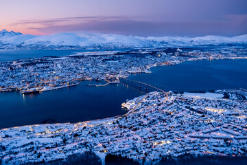 Aerial view of Tromso, Norway with city lights in winter from Storsteinen mountain at twilight. Tromsoya island with Tromso downtown, harbor, Sandnessundet bridge, fjord and mountains in polar night