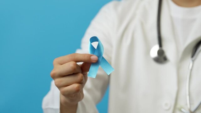 Young male doctor shows a blue ribbon, symbol of the fight against prostate cancer, human trafficking, the deaf community, blue background
