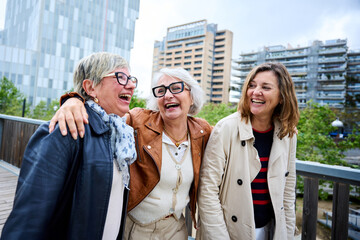 Three cheerful only mature Caucasian friends women enjoying walking happy together in urban park. Older gray hair tourists female people strolling laughing European sightseeing holidays outdoors 