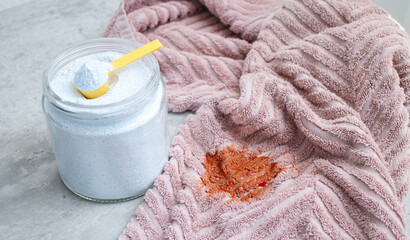 Close up of washing powder and a dirty pink towel with red stain on grey table. Cloth stain remover...