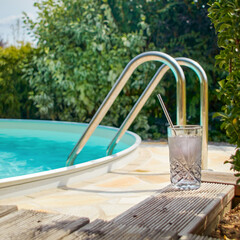a cool drink on a wooden terrace by the turquoise pool in front of green bushes