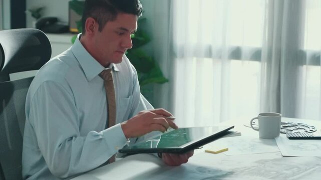 Professional engineer looking at phone while working on tablet with green screen at meeting table with turbine engine or jet engine sketch design and various metal gear scatter around. Alimentation.