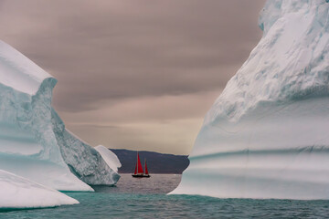 red sailboat between two icebergs in Disko bay off the western coast of Greenland