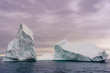 2 large icebergs in Disko Bay on the western coast of Greenland with a cloudy background