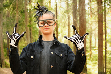 portrait of thoughtful teenage girl in total black halloween outfit in forest or park, kid making faces, copy space