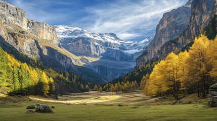 Fototapeta premium A stunning view of a mountain valley with snow-capped peaks, golden trees, and a grassy meadow.