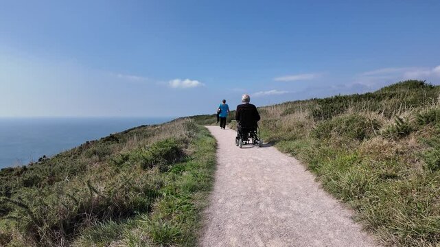 Devon England UK. 30.09.2024. Video. Elderly man using an electric wheelchair along a coastal pth in south Devon UK.