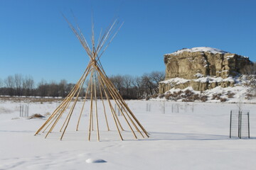 tipi sticks infront of a rock formation on a snowy blue sky day teepee tepee