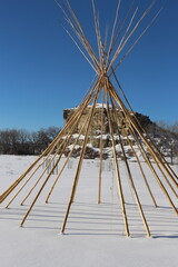 tipi sticks infront of a rock formation on a snowy blue sky day teepee tepee