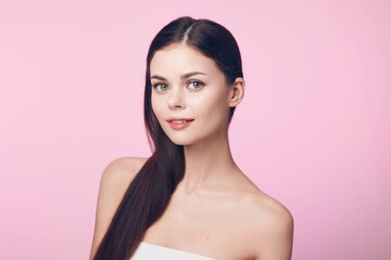 Beautiful young woman with long brown hair posing on a pink background with a white towel over her head, creating a serene and stylish image
