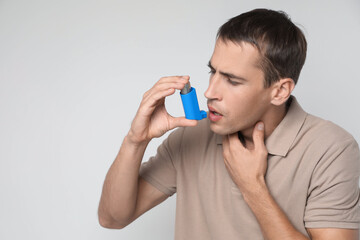 Man using asthma inhaler on light background