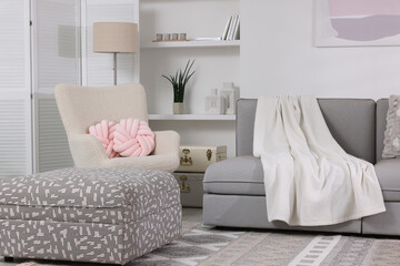 Comfortable sofa with blanket, armchair and folding screen in living room. Interior design