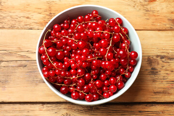 Fresh red currants in bowl on wooden table, top view