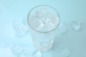 Refreshing water in glass with ice cubes on light blue background, closeup