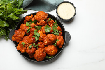 Baked cauliflower buffalo wings in baking dish, parsley and sauce on white marble table, top view. Space for text