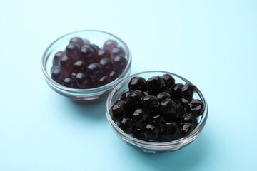 Dark tapioca pearls in bowls on light blue background, closeup