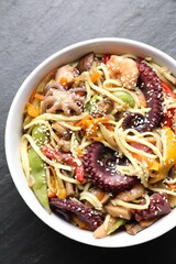 Stir-fry noodles with sea food in bowl on grey textured table, top view