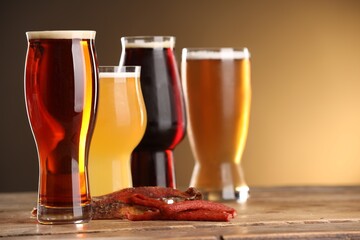Glasses with different types of beer and snacks on wooden table against color background, closeup