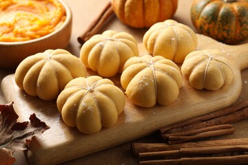 Raw pumpkin shaped buns and ingredients on brown table, closeup