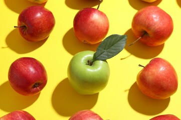 Green apple surrounded by red ones on yellow background, above view