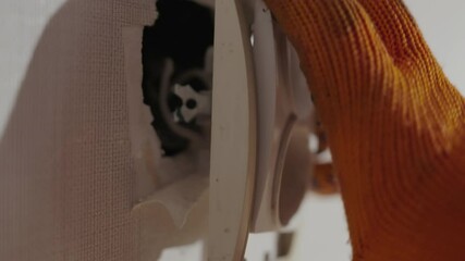 Close-up: Electrician's Orange-Gloved Hand Examining Malfunctioning Two-Plug Socket Hanging from Wall Wires | Professional Safety Inspection and Diagnostic of Faulty Electrical Outlet