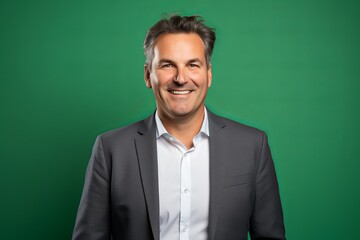 Handsome middle aged man with grey hair smiling and looking at camera against green background - Powered by Adobe