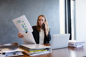 Fototapeta premium Focused Businesswoman Reviewing Reports and Handling a Phone Call in a Professional Office Setting