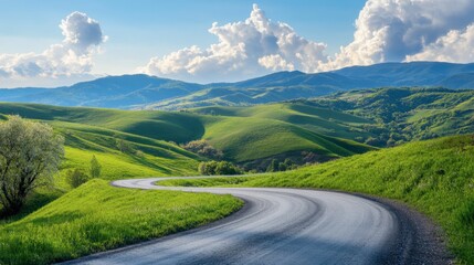 A curving asphalt road through green hills and mountains, under a clear sky with white, fluffy clouds on a sunny afternoon.