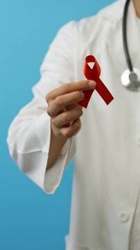 Vertical video, Young male doctor shows a red ribbon, symbol of the fight against VIH/SIDA, against drugs, blue background