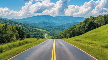 Fototapeta premium A scenic asphalt road leading into green hills and mountains, with a bright blue sky and soft, white clouds overhead.