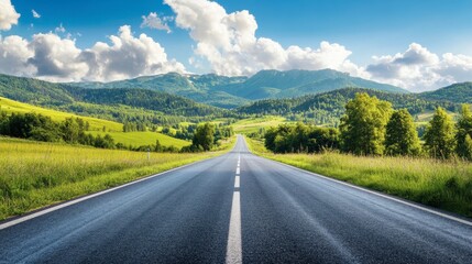 Fototapeta premium A scenic asphalt road leading towards green mountains, under a bright sky with soft, scattered clouds on a sunny day.
