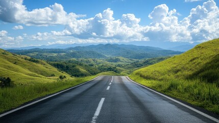 Fototapeta premium A scenic asphalt road through green hills and mountains, with a clear sky and puffy white clouds on a sunny day.