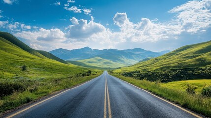 Naklejka premium A scenic asphalt road through green hills and mountains, with a bright sky and scattered, puffy clouds on a sunny day.