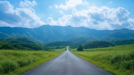 Naklejka premium A straight asphalt road leading into green mountains, with a bright sky and soft, fluffy clouds on a sunny, clear day.